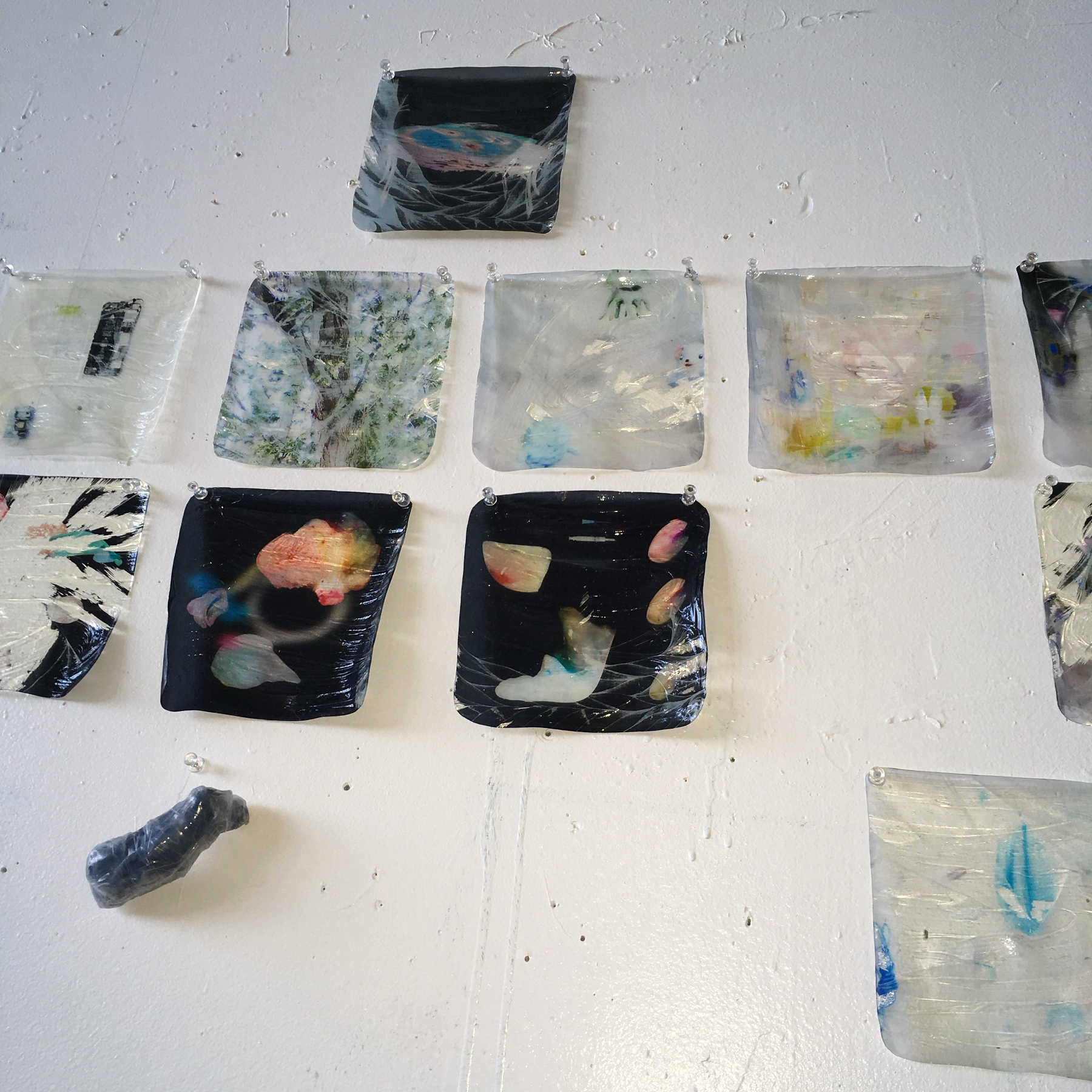 Several abstract artworks in various colors are displayed on a white wall.